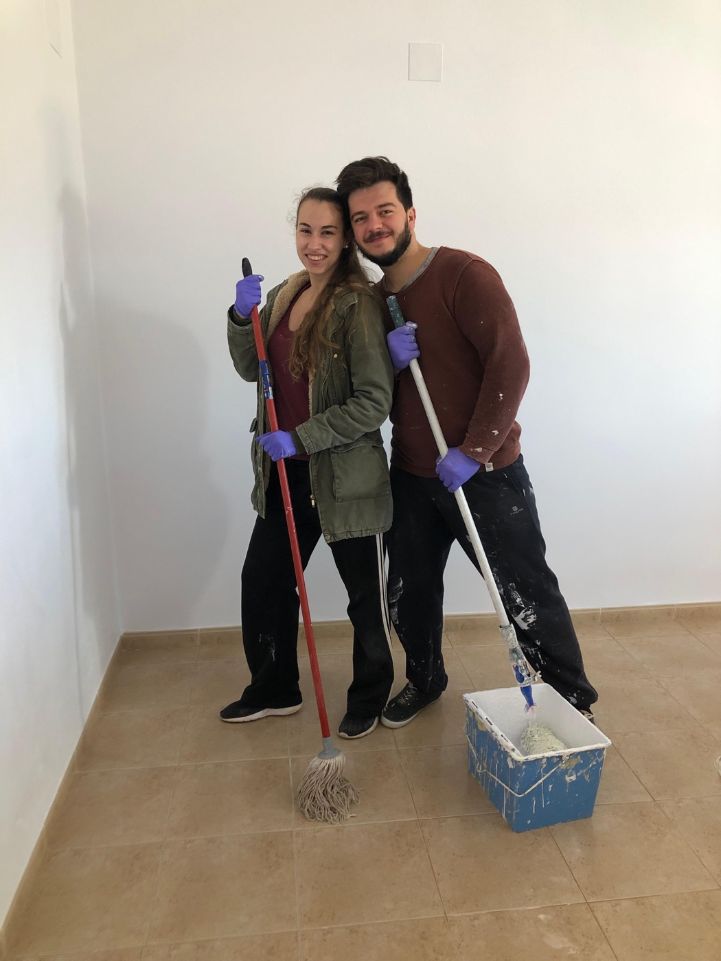 Raquel y Samuel con una escoba y una fregona en su casa vacía